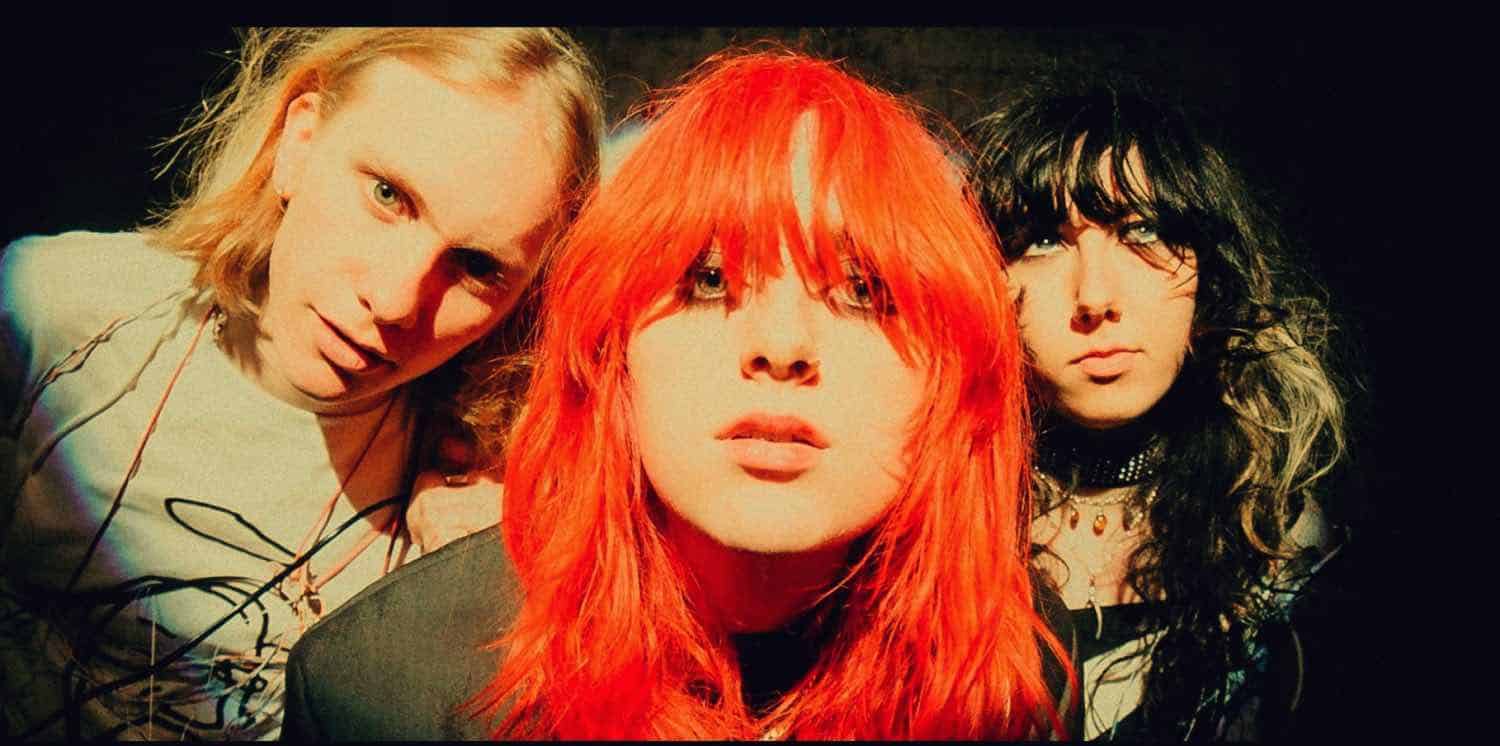 Vintage rock band with vibrant red-haired lead singer, indie style, on stage with moody lighting.