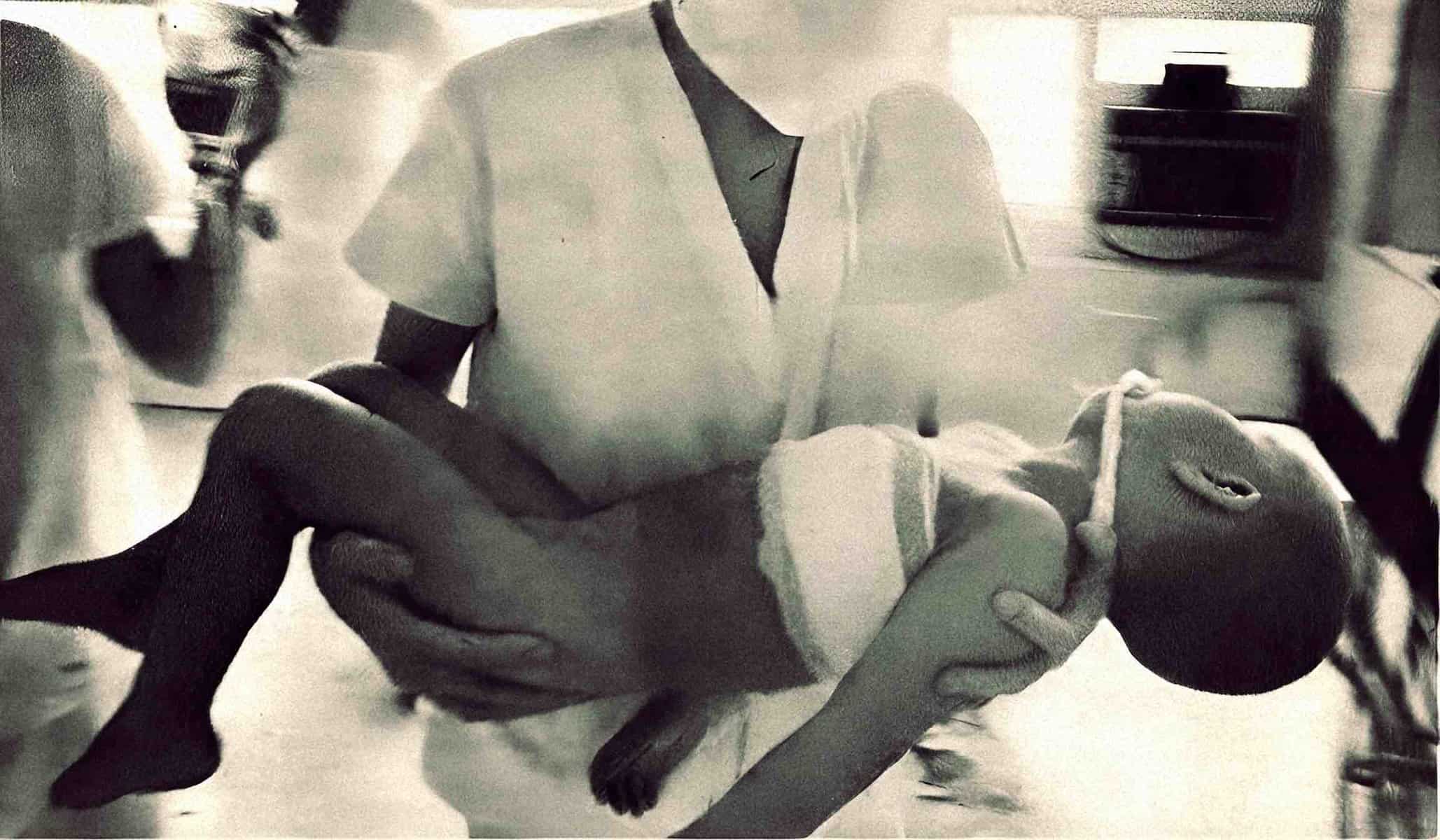 Baby dog being held by a person in a room with a white wall and furniture, captured in black and white, showcasing a moment of affection and care, with an emphasis on nostalgia, animals, and family bonds.