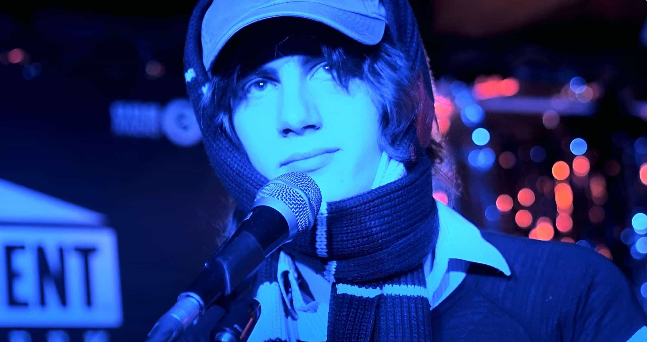 Youthful singer performing with microphone at live music event, vibrant city lights blurred in background.
