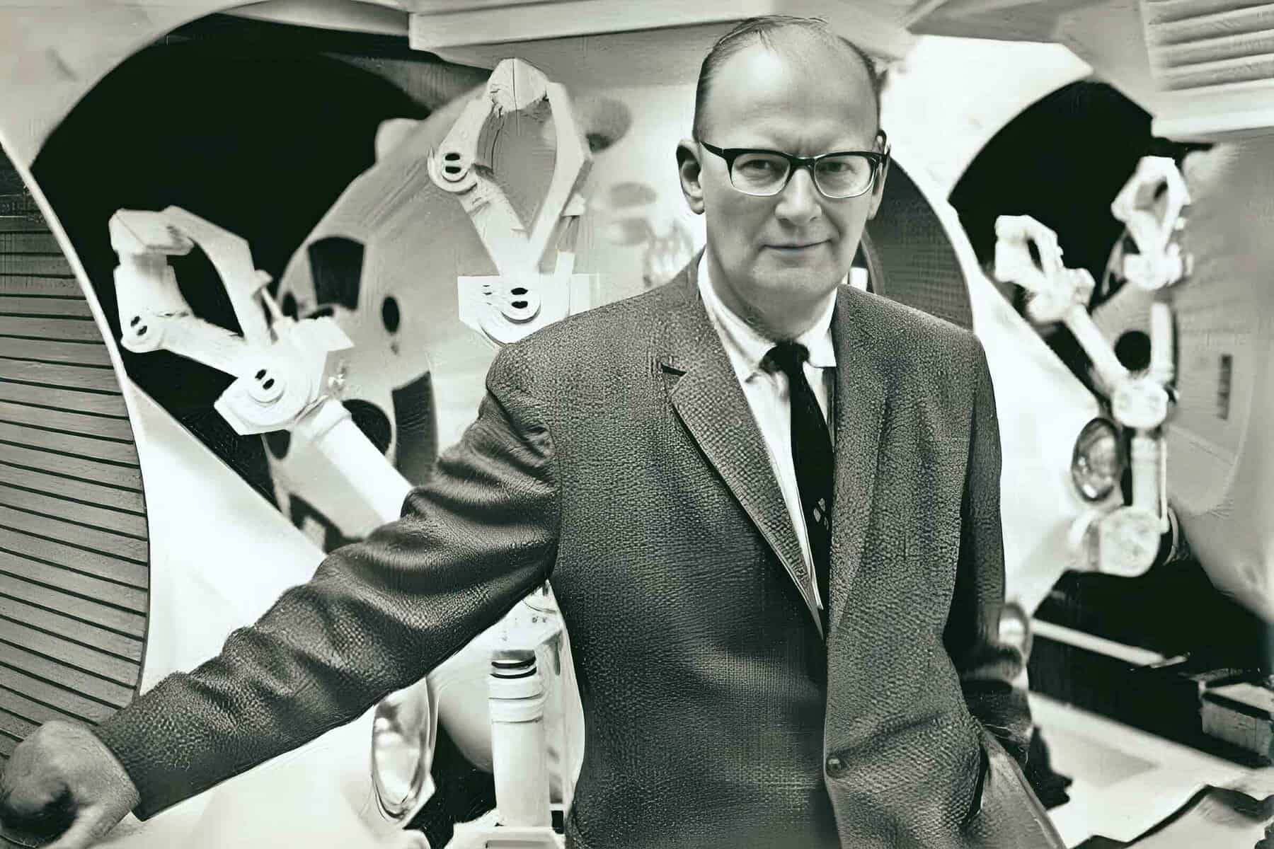 Vintage black and white photo of a man in a suit and glasses standing in front of a large reel-to-reel tape recorder, representing audio preservation and radio broadcasting, emphasizing historical news and music archives.