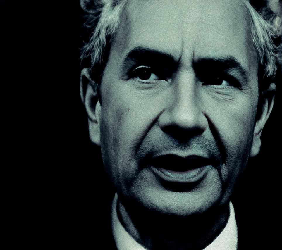 Portraying a distinguished older man with silver hair speaking passionately, capturing a moment of public speaking or narration that aligns with historical news archives.