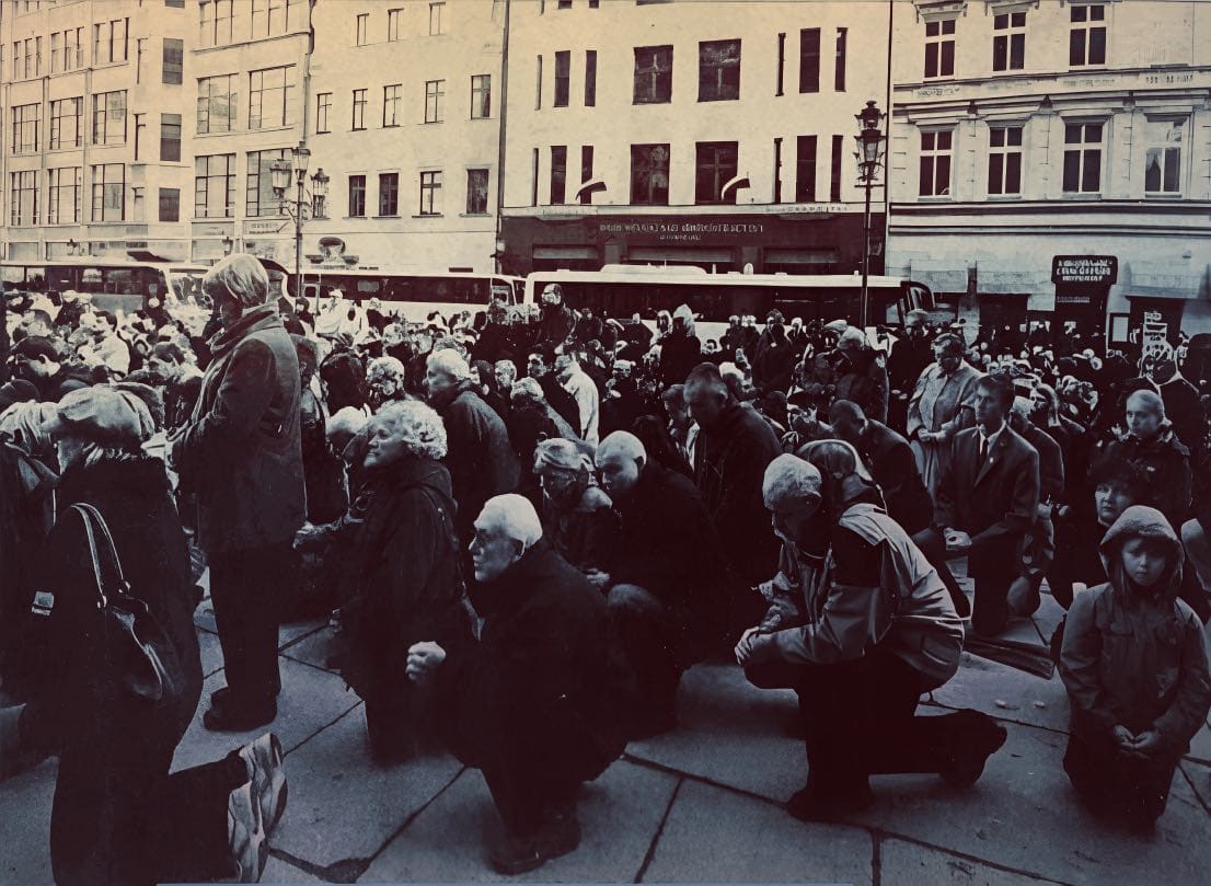 People praying and mourning on the street in a historical black and white photo, capturing a moment of collective grief and remembrance in an urban setting.