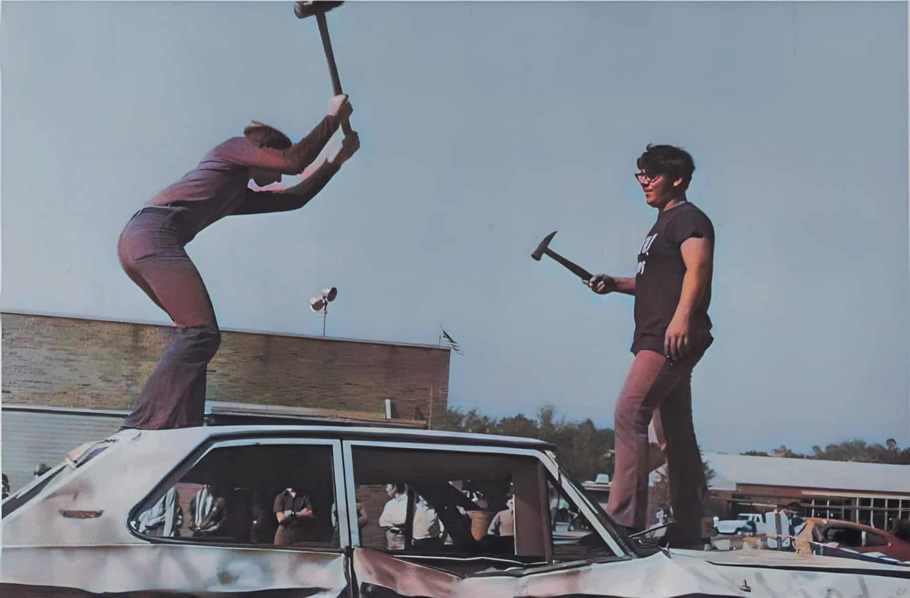 Climbers standing on a car roof and using hammers, symbolizing protest or activism, with a clear sky background.