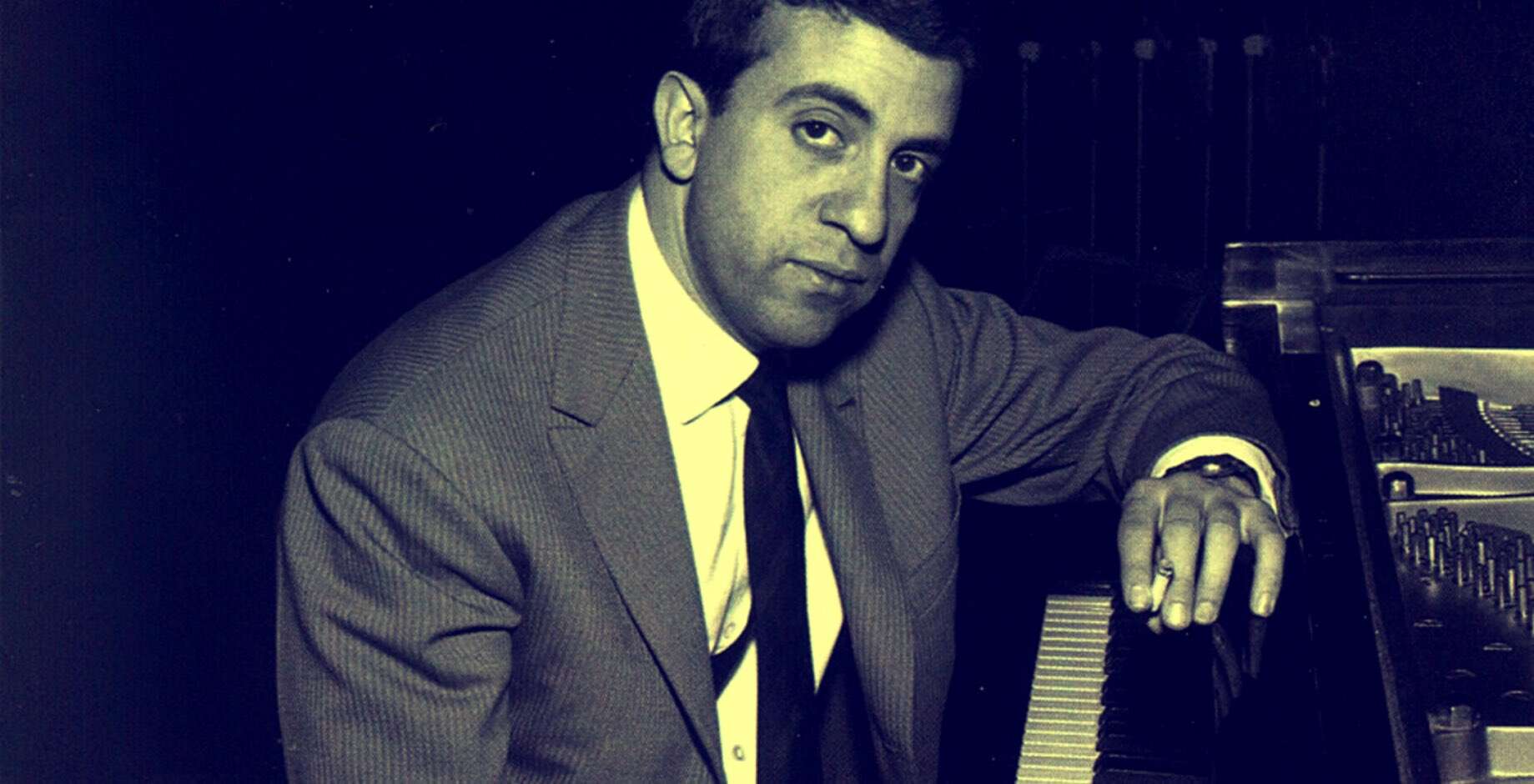 Vintage black and white photo of a man in a suit sitting at a piano, representing historical music recordings from Past Daily's sound archive.