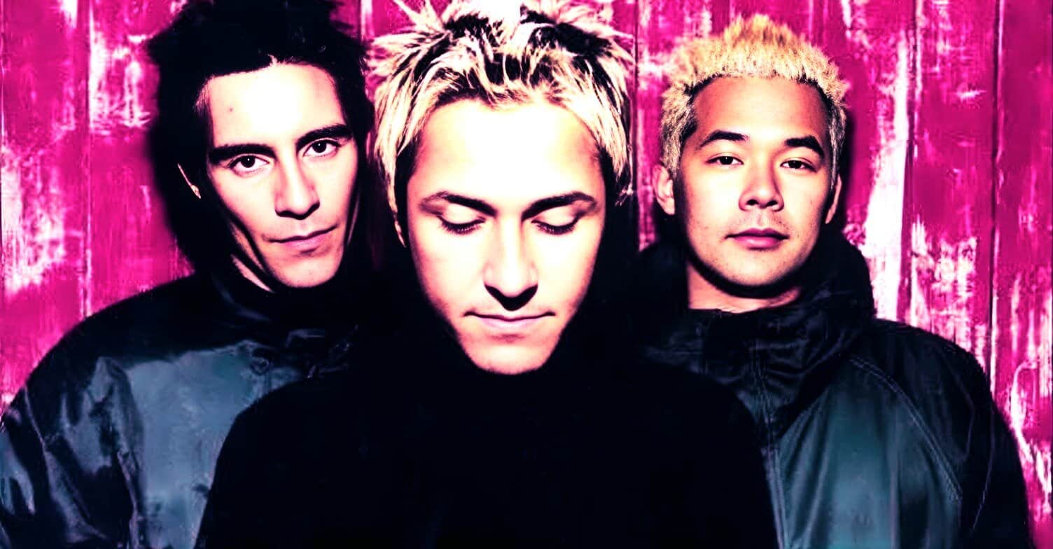 Young male music band members with dyed hair, modern fashion style, in front of pink textured background, representing news, history, and music archives.