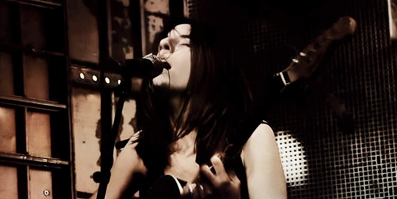 A woman singing passionately into a microphone during a live music performance, capturing the raw emotion and energy of the moment.