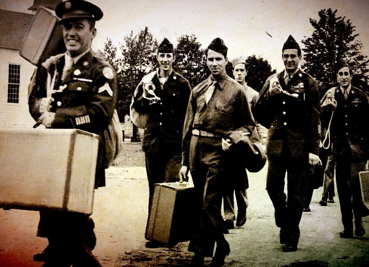 Soldiers walking with suitcases in a historic military photo, vintage black and white image, World War II era, soldiers smiling, carrying luggage, military uniforms, soldiers marching, wartime history, nostalgic military scene.