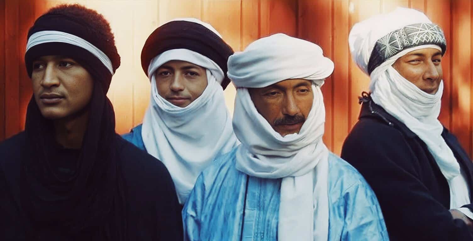 Men wearing traditional Moroccan djellabas and headscarves, standing against a wooden background, representing Moroccan culture and heritage.