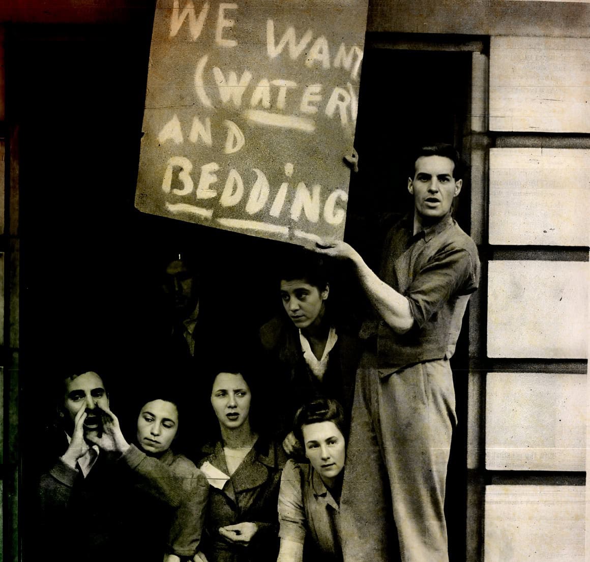 A vintage black-and-white photo showing a group of protesters, including a man holding a cardboard sign that reads "We Want Water and Bathing," emphasizing social activism and historical protest scenes.