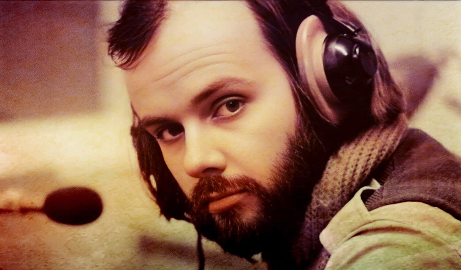 Headshot of a young man wearing headphones, capturing a moment of music or radio broadcasting, emphasizing audio history, news, and cultural archives.