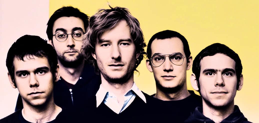 New york times band photo, indie rock band with five members posing, casual style, yellow background, music history, classic rock, musical archive, past daily, sound archive, music history, news and culture, nostalgia, historical music archive.