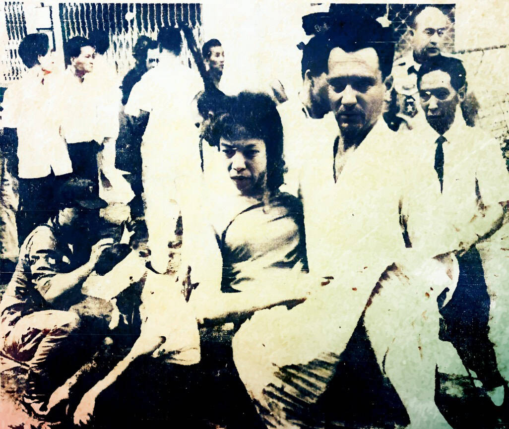 Vintage black and white photograph of a lively group of people, including a woman and men in white shirts, capturing a moment of social gathering or celebration.