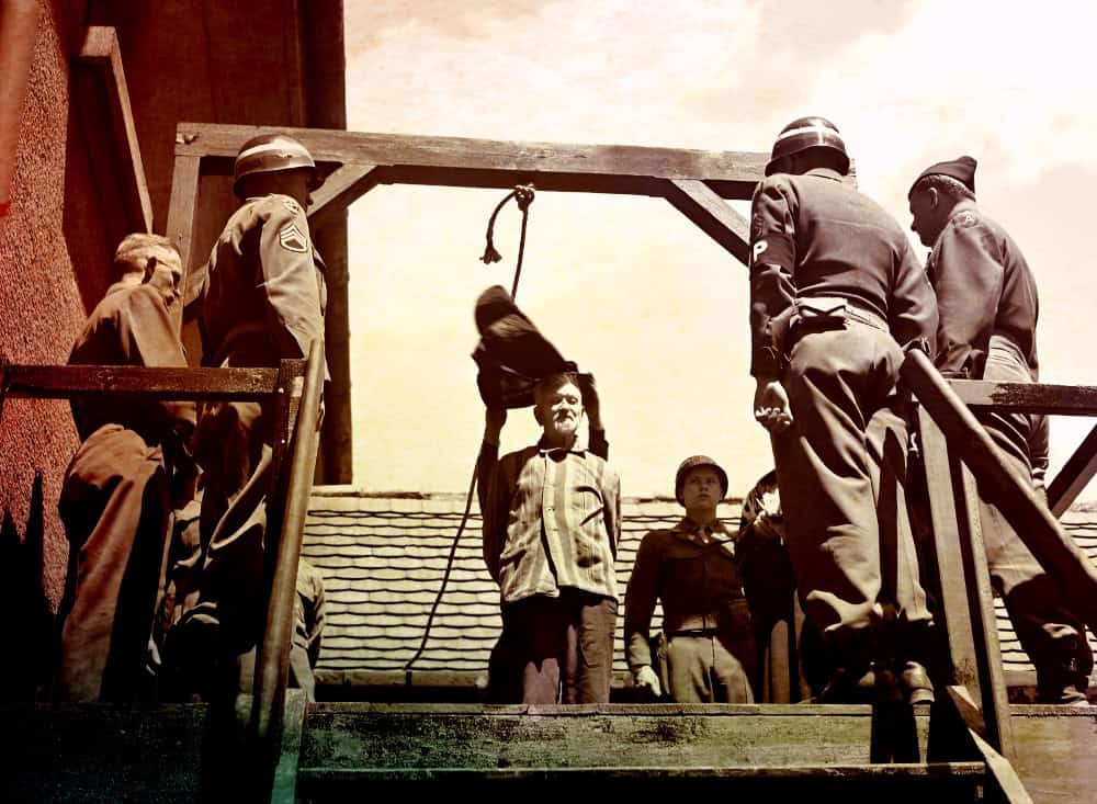 Guinea pig hanging from noose on wooden gallows with Imperial Japanese officers and civilians witnessing execution, historical photo.