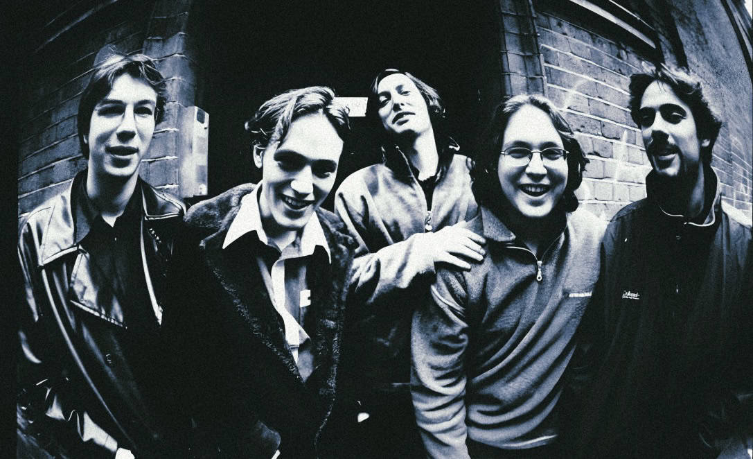 Urban band members standing outside brick building, black and white photo.