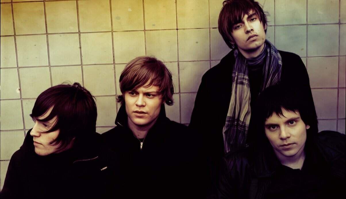 - Young male band members with dark hair posing against a tiled wall, capturing indie music scene.