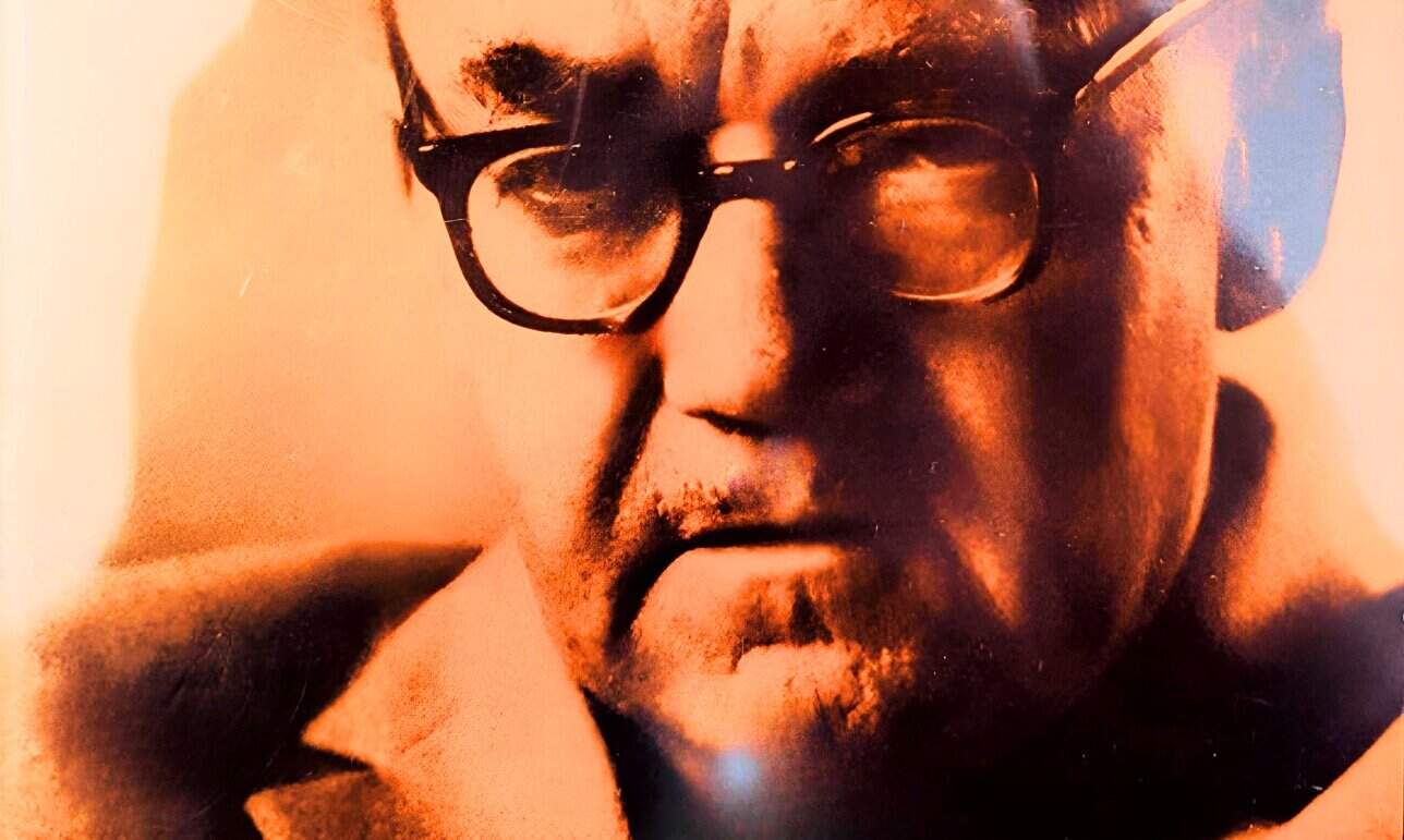 Vintage black and white photo of a serious man wearing glasses, representing historical news archives and famous personalities in a sound archive related to news and music.