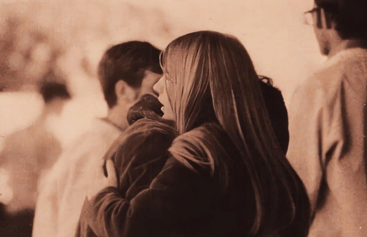 A woman and a man share an intimate moment in a sepia-toned photograph, capturing a nostalgic scene of love and connection at a social gathering or public event.