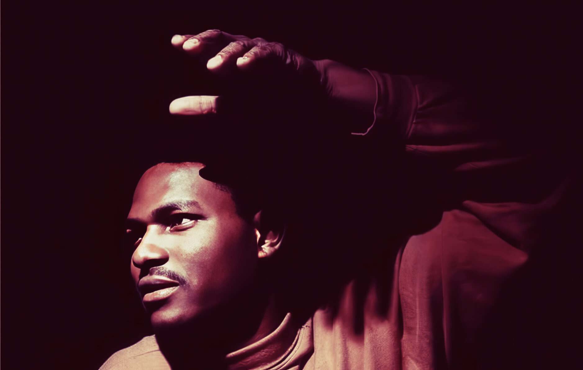 Young man with short hair, looking thoughtfully into the distance, raising his hand and shielding his eyes, artistic portrait with dark background, emphasizing music, history, and news archive themes.