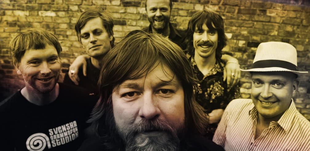 Past daily sound archive of news history and music with a band of six smiling men in front of a brick wall, capturing the essence of vintage music recordings and historical sound clips.