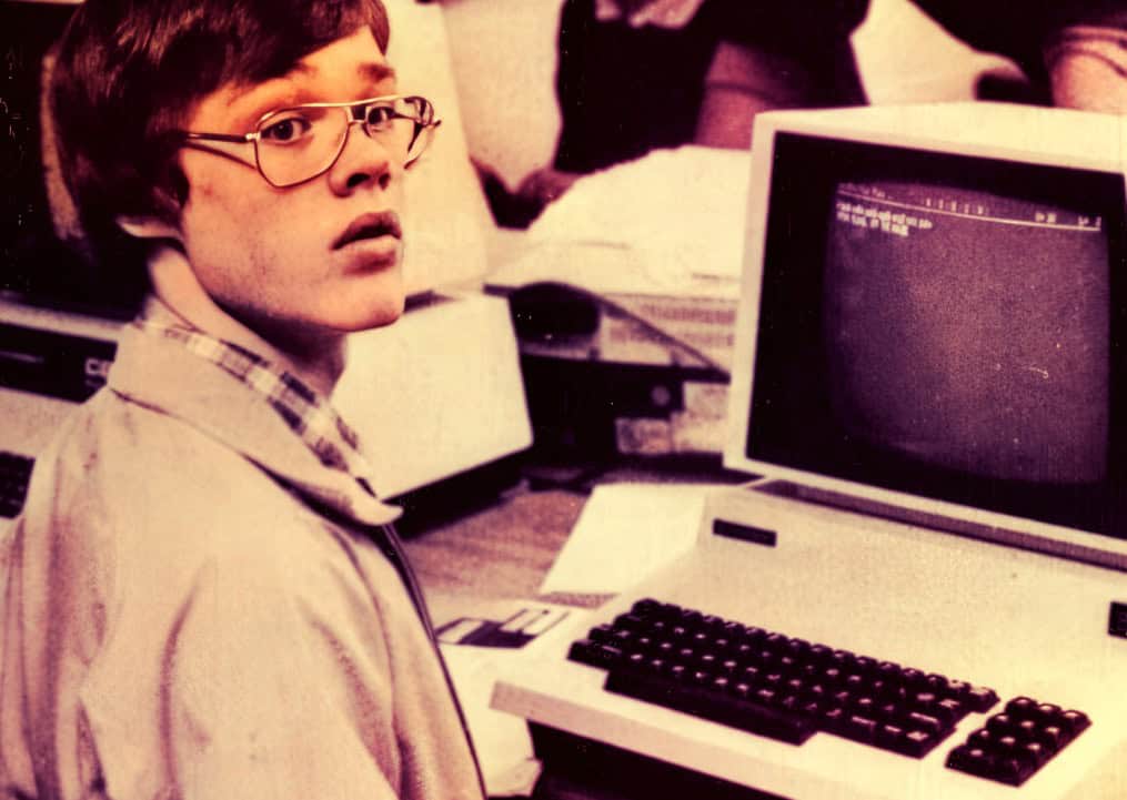 Young boy using an early home computer with a CRT monitor, keyboard, and audio equipment, representing vintage technology for news, music, and historical sound archives.