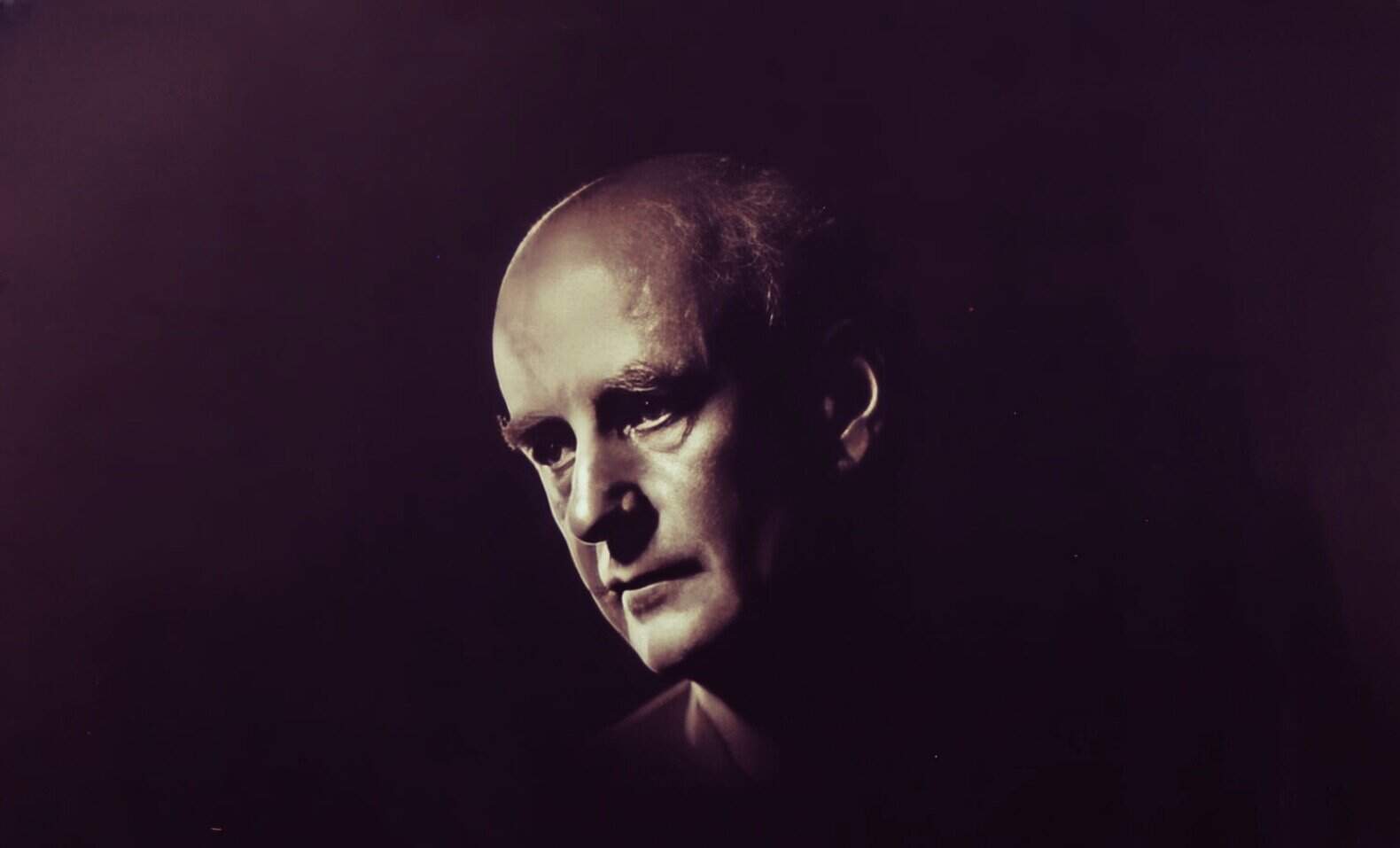 Eerie portrait of a man with a bald head and intense expression, dark background emphasizing moody atmosphere, inspired by historical and cultural themes, perfect for news, history, and music archives.