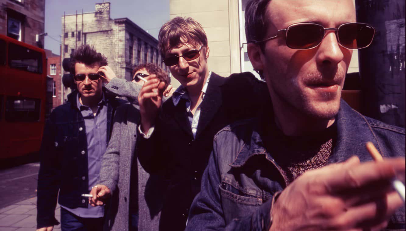 Smoky-eyed men in sunglasses on city street, punk style, 1980s fashion, urban scene, vintage photo of music culture, classic rock, nostalgic street photography, Past Daily archive relevance.