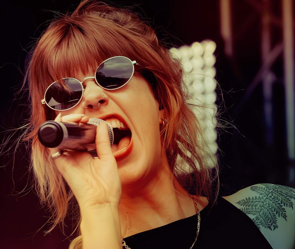 Female singer with red hair and sunglasses performing passionately at a concert, holding microphone, rock music, live performance, music artist, stage presence, music festival, energetic vocals, rock concert ambiance, Past Daily archive relevance.