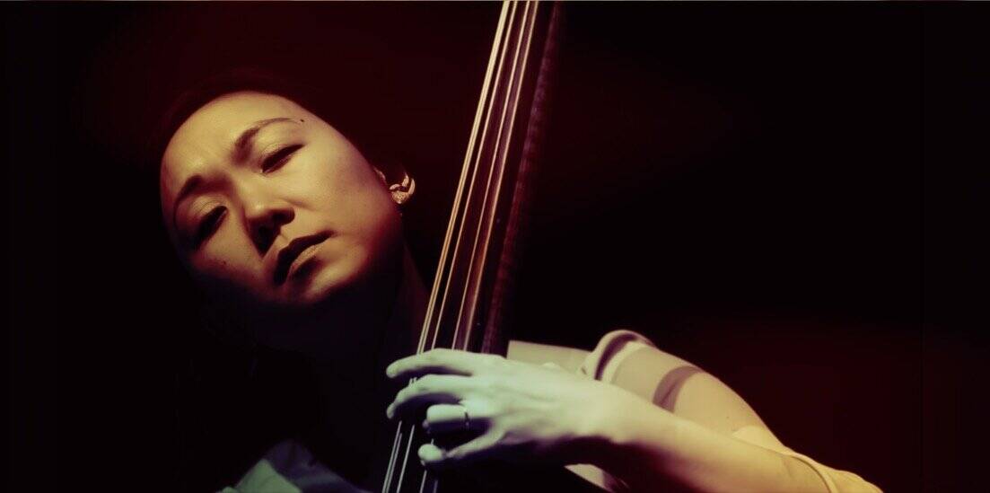 Elegant female jazz musician with a double bass, performing passionately in a dark stage setting. Perfect for vintage music archives and classic jazz artist features.