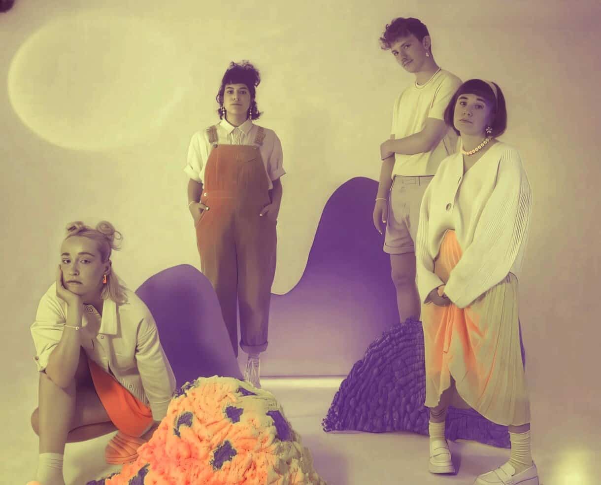 Colorful vintage-inspired aesthetic photo of four young women with unique hairstyles and outfits, set against a pastel background with artistic props, perfect for music, fashion, and 80s retro themes.