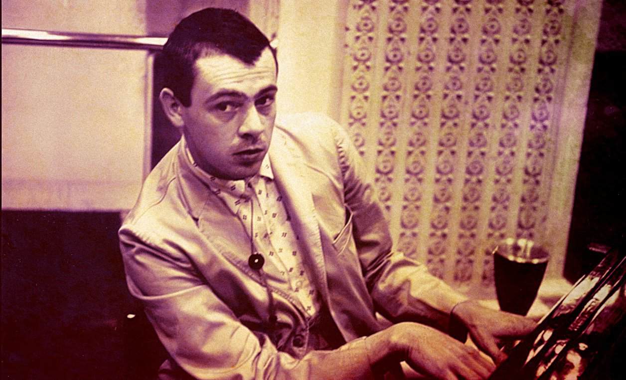 A black-and-white photo of a young man playing piano in a vintage recording studio, capturing the essence of classic music and historic radio broadcast environments.