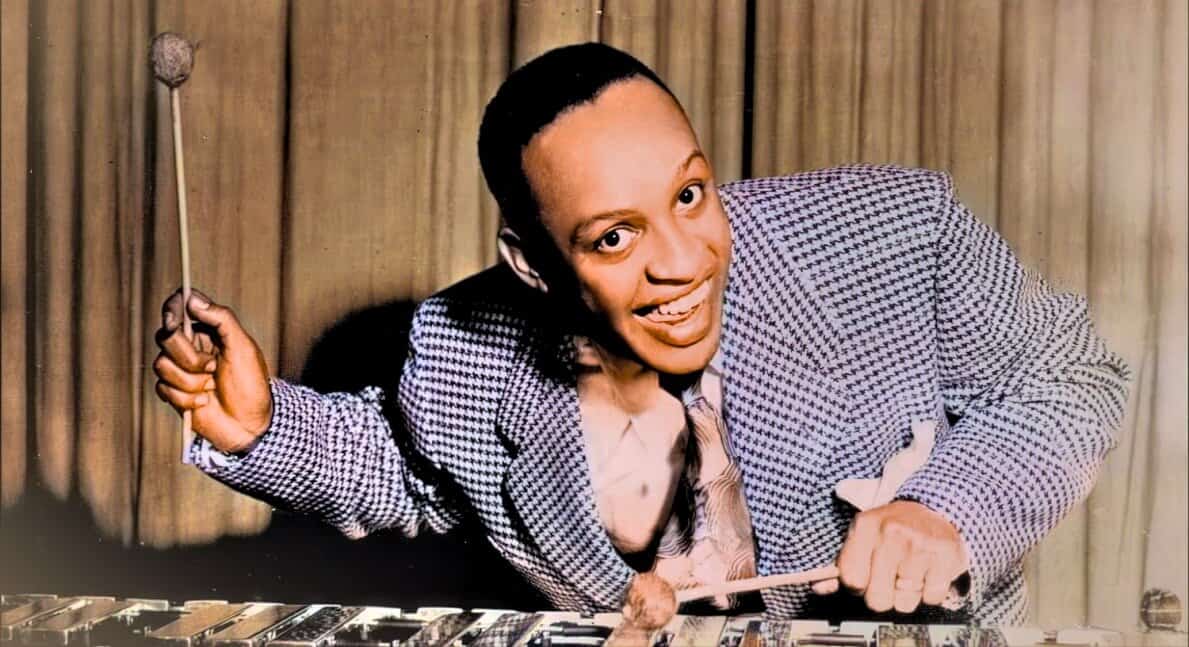 Xylophone player in vintage jazz performance, joyful musician in checkered blazer, classic sound archive image, historic music scene, past daily news, sound archive of news and music, vintage music and history image, jazz musician with xylophone, retro music scene revival, historic jazz music recording.