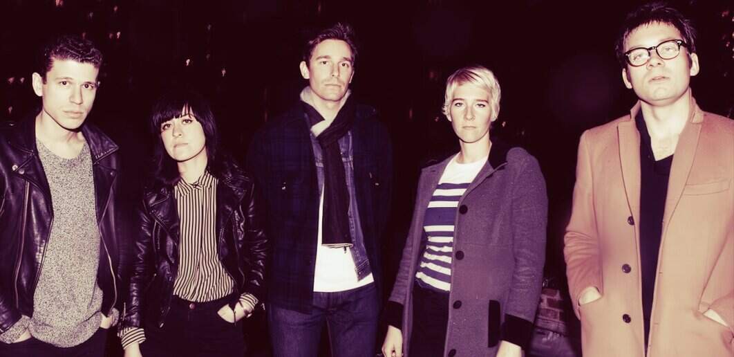 A black and white photo of a five-member indie band posing outdoors at night, dressed in casual and vintage-inspired clothing, showcasing their distinct styles.