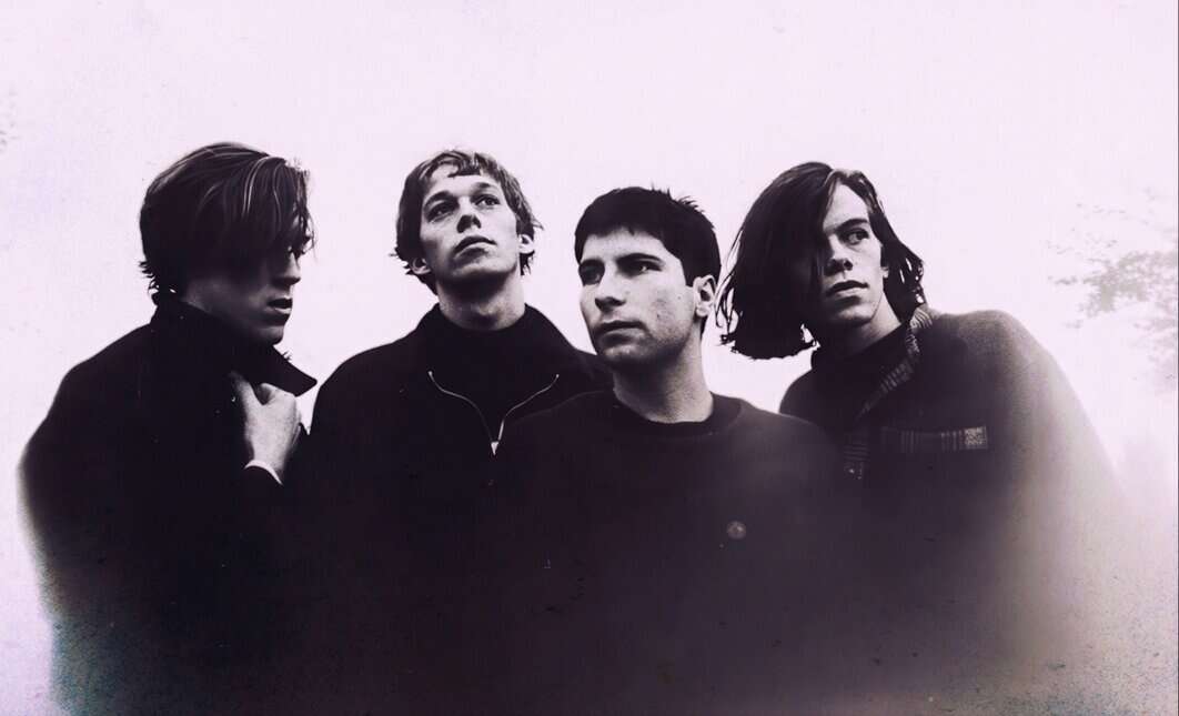 Vintage black and white photo of a rock band with four members, showcasing their moody expressions and distinct hairstyles, emphasizing music, history, and cultural influence.