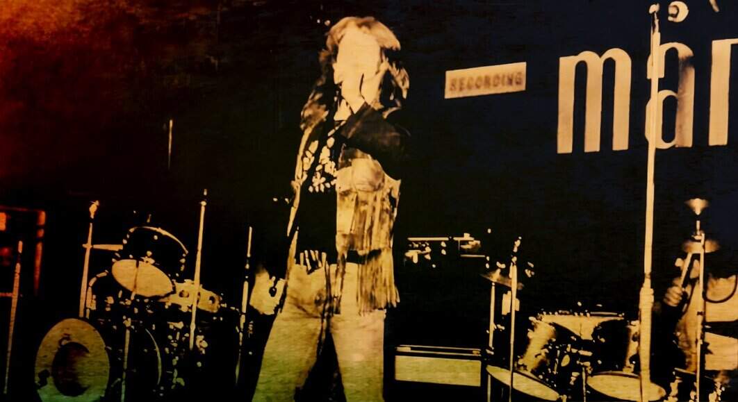 An image of a jazz vocalist performing on stage with drums and microphones at a live music event in a dimly lit venue.