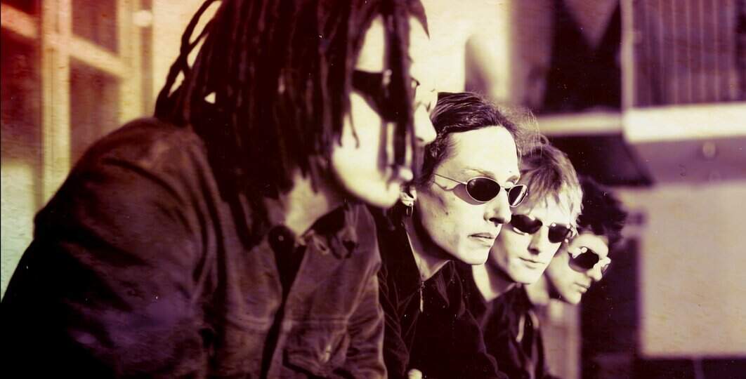 Hip-hop band members with sunglasses sitting outdoors, vintage style, music and news archive, Past Daily focus on history and cultural recordings.