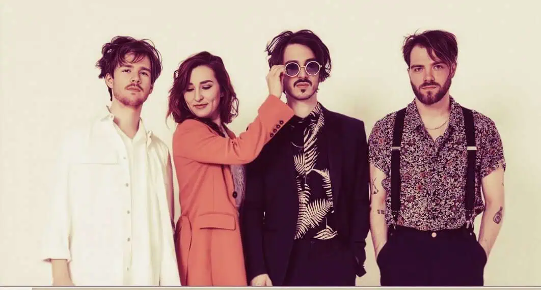 Vintage indie band portrait, four members with trendy hairstyles and attire posing against a plain background. Perfect for music and culture archives, highlighting modern musical artists and styles.