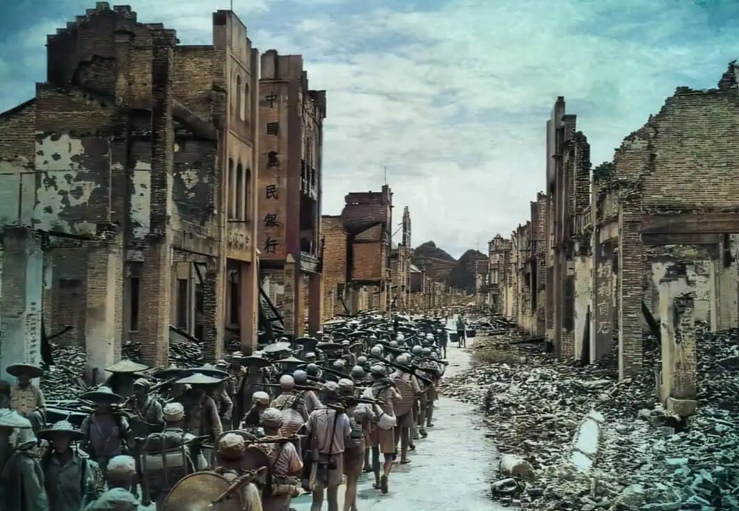 Ruined street with destroyed buildings and a line of soldiers walking through, depicting a historical war aftermath scene.