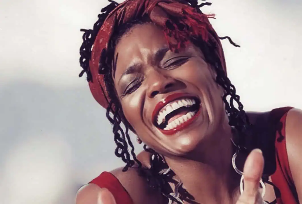 Vibrant portrait of a woman with red dreadlocks and bold makeup, smiling joyfully, capturing a moment of happiness and expressive energy.