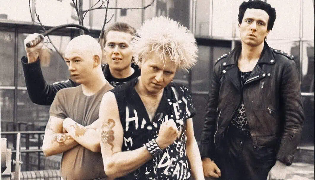 B-52s punk rock band members with distinctive 1980s hairstyles and leather jackets posing outdoors in an urban setting.